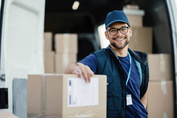 Portrait of happy worker unloading boxes from a delivery van and looking at camera.